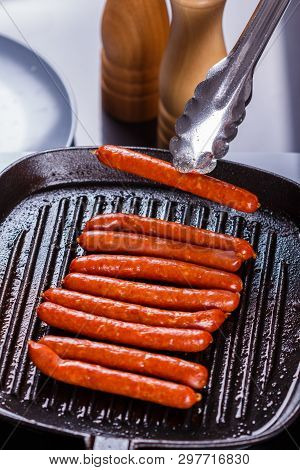 Young Woman In A Gray Apron Fries Sausages