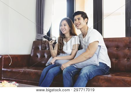 Happy Asian Young Couple Loving On The Couch Watching A Movie Together,woman Holding Remote And Her 