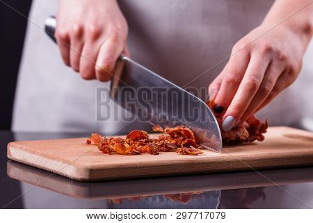 Young Woman In A Gray Apron Cuts Roasted Bacon