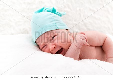 Crying Newborn Baby Without Clothes And In A Cap On White Pillows.