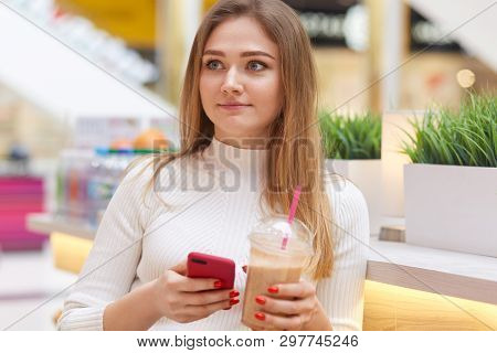Portrait Of Beautiful Girl, Has European Appearance, Dressed White Sweater, Sits In Cafe, Drinks Lem