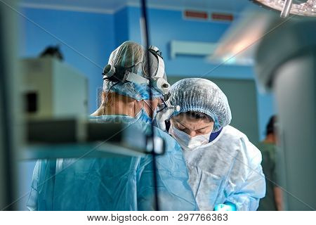 Surgeon Performing Cosmetic Surgery In Hospital Operating Room. Surgeon In Mask Wearing Loupes Durin