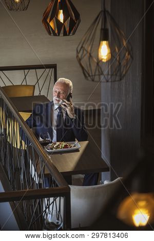 Senior Businessman Taking A Break, Having Lunch In A Restaurant And Apeaking On The Phone