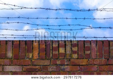 Barbed Wire And Brick Wallagainst The Blue Sky. The Blue Sky Is Covered With Barbed Wire. Prison And