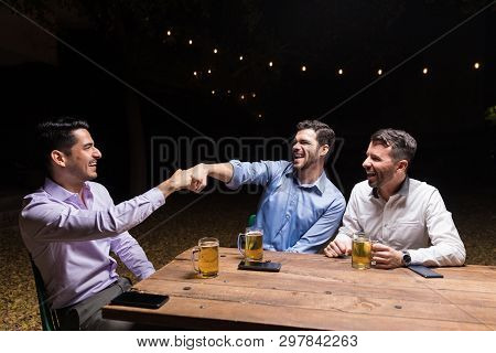 Cheerful Male Besties Bumping Their Fists While Enjoying Beer At Backyard Party During Night