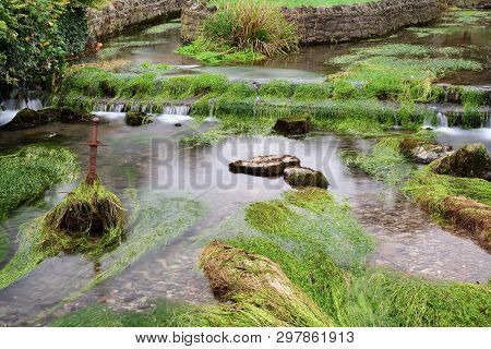 Long Exposure Of The River Flowing Past A Sword Sticking Out Of The River In  Cheddar Village In Som