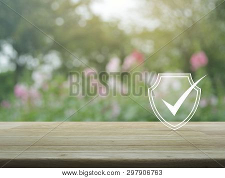 Security Shield With Check Mark Flat Icon On Wooden Table Over Blur Pink Flower And Tree In Garden, 