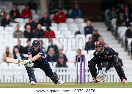 LONDON, ENGLAND. 25 APRIL 2019: Nick Gubbins of Middlesex plays a shot as wicketkeeper Ben Foakes of Surrey looks on during the Surrey v Middlesex, Royal London One Day Cup match at The Kia Oval. 