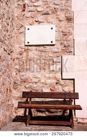 White Marble Sign. White Marble Sign On A Stone Wall. There Is Also A Brown Wooden Bench To Sit And 
