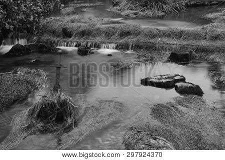 Long Exposure Of The River Flowing Past A Sword Sticking Out Of The River In  Cheddar Village In Som