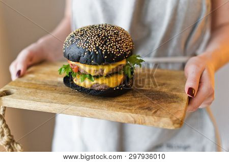 Girl Chef Holds In Her Hands A Wooden Cutting Board With A Black Cheesburgers.