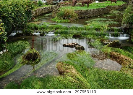Long Exposure Of The River Flowing Past A Sword Sticking Out Of The River In  Cheddar Village In Som