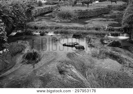 Long Exposure Of The River Flowing Past A Sword Sticking Out Of The River In  Cheddar Village In Som