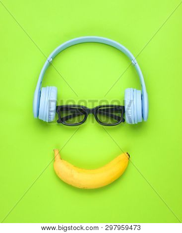 Minimalism Flat Lay Concept. Smiling Face Listens To Music Headphones, 3d Glasses, Banana On A Green