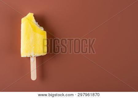 Yellow Popsicle With Some Bites On A Chocolate Brown Background
