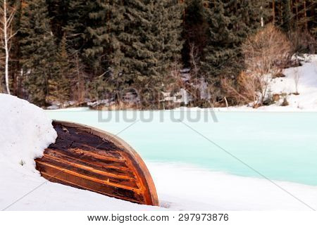 Old Wooden Destroyed Flooded Fishing Boat Lie In Snow On Shore Of Ice-covered Frozen River In Winter