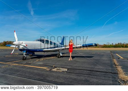 A gorgeous young blonde model poses outdoors with a single engine aircraft at a local airport