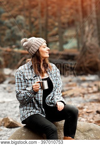 Woman Drinking Coffee On The Riverbank  In The Forest