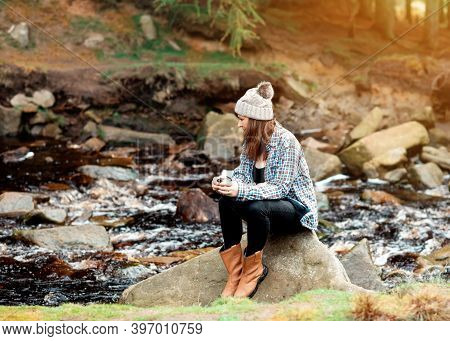 Happy Woman Drinking Coffee On The Riverbank  In The Forest
