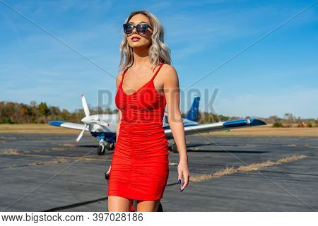 A gorgeous young blonde model poses outdoors with a single engine aircraft at a local airport