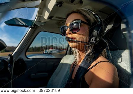A gorgeous young blonde model poses outdoors with a single engine aircraft at a local airport