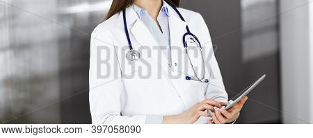 Unknown Woman Doctor Iusing Tablet Computer In Her Hands, While Standing In Clinic. Medicine Concept