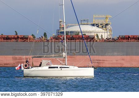 Swinoujscie, West Pomeranian - Poland - 2020: The Yacht Sailing Along The Port Canal Against The Shi