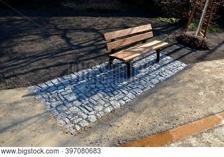 Wooden Park Bench With A Metal Frame In A Park On A Rectangle Stone Granite Pavement. Design Element