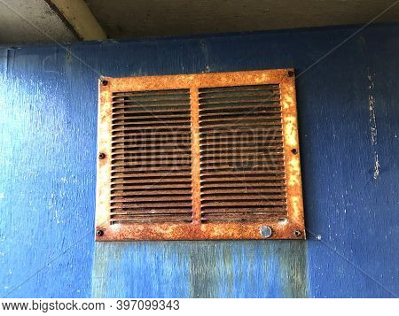 A Close Up View Of A Rusted Airvent On A Solid Blue Door