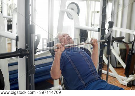 Elderly Male Is Having Intense Workout In Gym. Senior Caucasian Man Lifting Weights At Fitness Club.