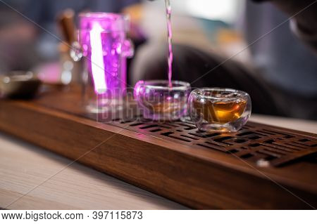 A Man Passes Hot Amber Tea From A Glass Flask Into A Cup. To Preserve Its Strong Flavor. Bamboo Tray