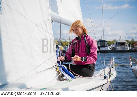 Womens River Regatta On A Sunny Day. A Young Blonde Sets Up The Rigging And Secures The Genaker Sail