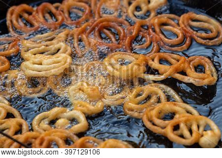 Frying Jalebi Batter In Oil. Red And Orange-colored Batter Will Be Dipped Into Sugar Syrup For A Swe