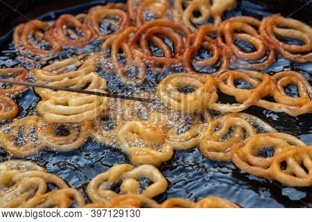 Frying Jalebi Batter In Oil. Red And Orange-colored Batter Will Be Dipped Into Sugar Syrup For A Swe