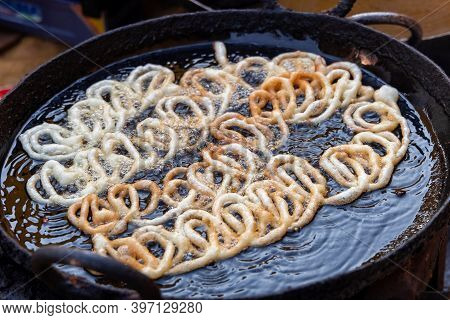 Frying Jalebi Batter In Oil. Red And Orange-colored Batter Will Be Dipped Into Sugar Syrup For A Swe