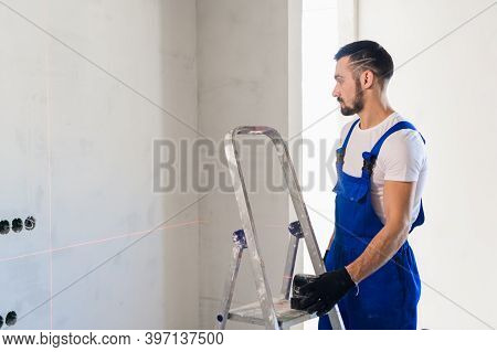 The Handyman Put The Laser Level On The Ladder And Looks At The Markings On The Wall