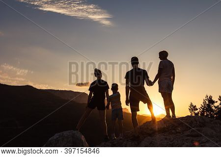 Happy Family Together In Mountains At Sunset Holding Hands Looks Into Distance. Back View Of Silhoue