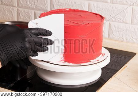 The Gloved Chef Levels The Cake With Red Cream With A Spatula.