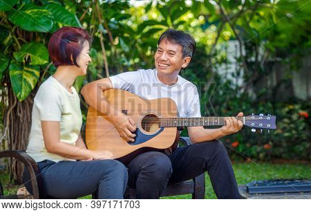 Middle Aged  Couple Playing Guitar While Relax Sitting On Bench In Backyard.