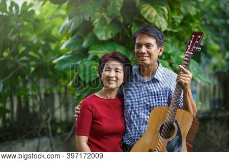 Middle Aged  Couple Playing Guitar While Relax Sitting On Bench In Backyard.