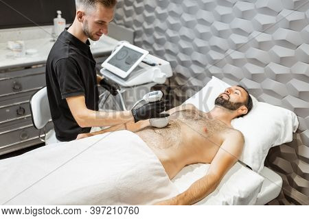 Man During An Ultrasound Liposuction Procedure At Luxury Spa Salon. Doctor Working On Abdomen Area