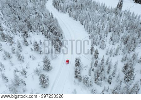 Drone view of a red car driving though a snowy forest in Lapland, Finland 