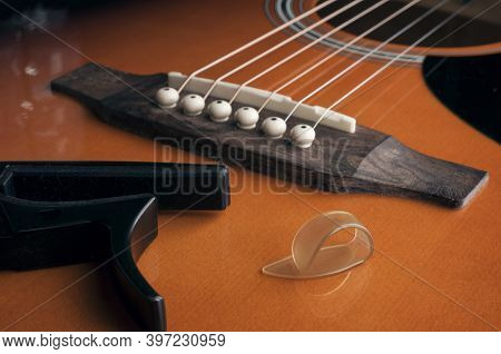 Fingerpick Guitar Concept: A Thumb Pick And A Guitar Capo Laying On Acoustic Guitar
