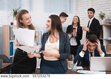 Two Young Girls Are Laughing At Work Annoying Boss. Two Women Are Standing In The Office With Papers