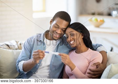 Smiling Future Mom And Dad With Positive Pregnancy Test Waiting For Their Baby At Home. Young Black 