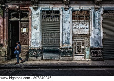 Havana, Cuba, July 2019, woman walking in front of a dilapidated building with the closed cafeteria `Cuba y Costa` in the old part of the city
