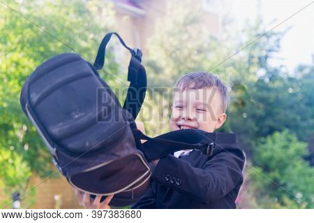 A Teenage Boy Is A European Schoolboy In A Black Suit, White Shirt. The Student Takes Off His Backpa