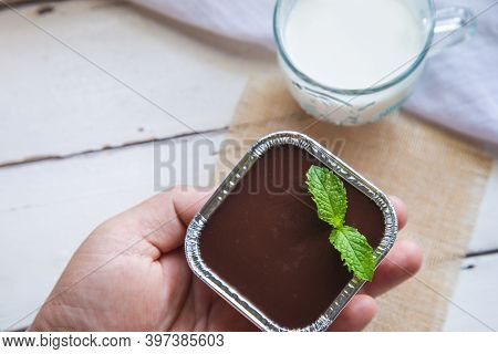 Top View Chocolate Fudge Cake With Peppermint In A Man Hand With A Cup Of Milk On White Wooden Table