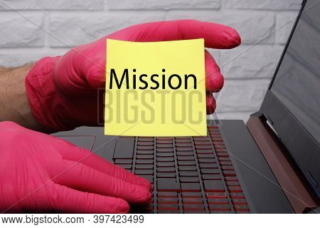 The Words Mission On Yellow Paper In A Mans Red-gloved Hand.