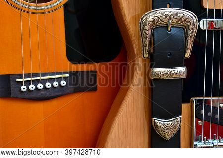 Acoustic And Electric Guitars And Leather Strap With Silver Buckle Close-up.